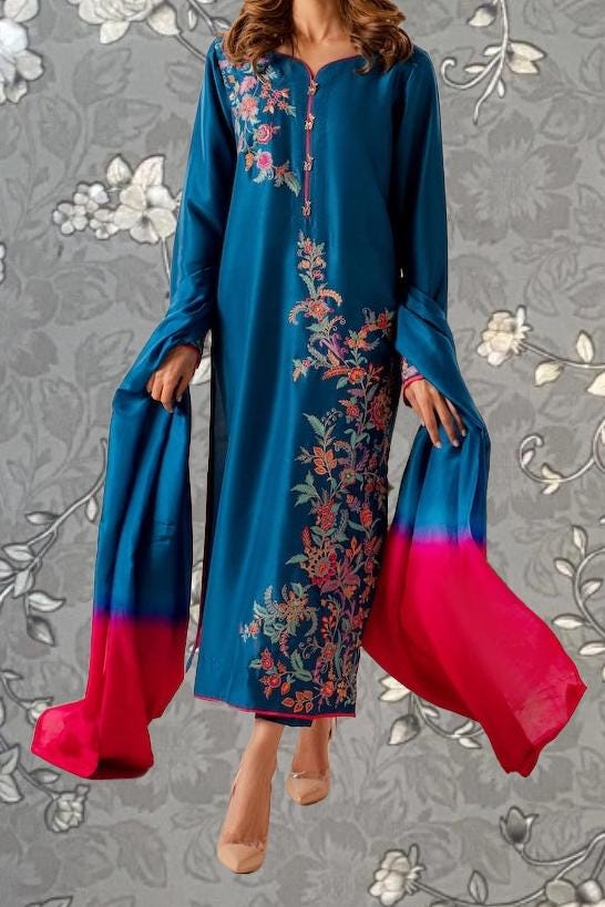 A woman wearing a long blue dress with floral embroidery and a matching red shawl is shown against a gray floral background.