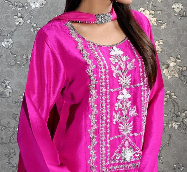 A close-up of a woman wearing a bright pink dress with intricate embroidery and a matching pink scarf.