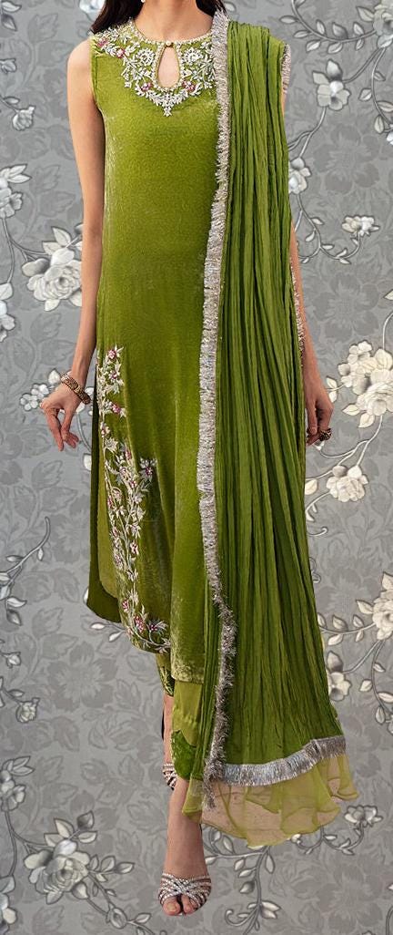 A woman wearing a green dress with a matching green shawl, standing against a gray floral background.