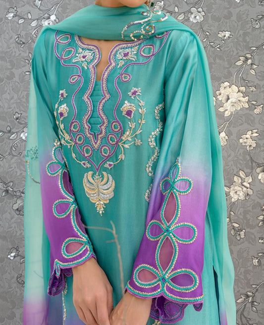 A close-up of a person wearing a turquoise and purple dress with intricate embroidered patterns.