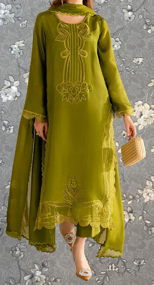 A woman wearing a long, green dress with intricate embroidery and lace details, standing against a gray floral background.