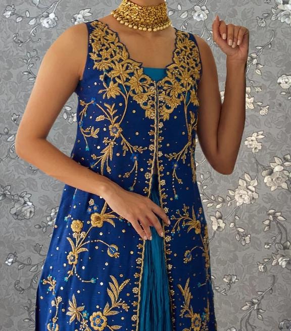 A woman wearing a blue and gold dress with intricate embroidery and a gold choker necklace.