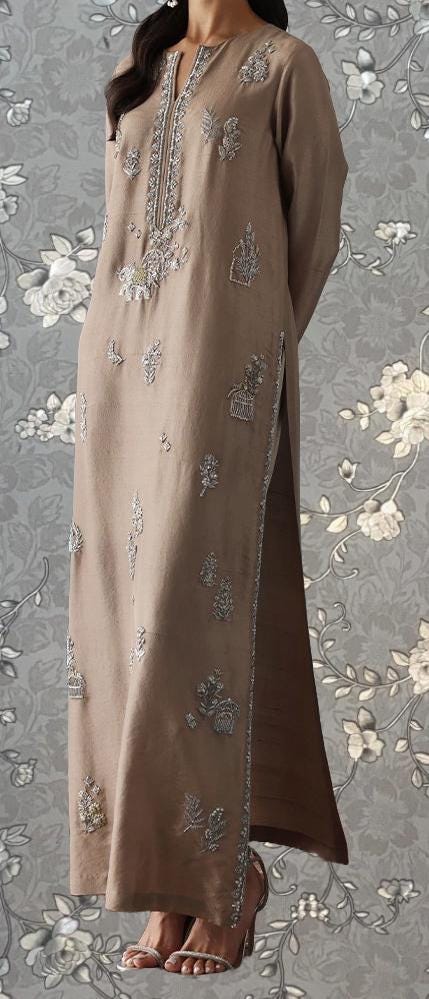 A woman wearing a long, beige dress with intricate embroidered designs on the front and sides.