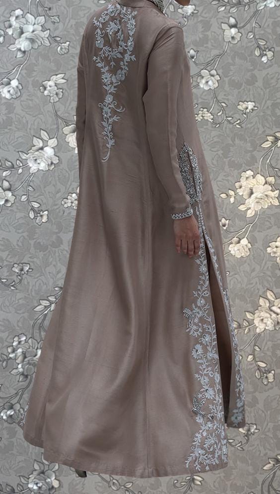 a person wearing a long, beige dress with intricate embroidered designs on the back and sides.