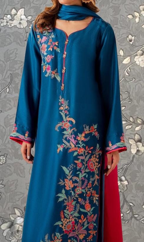 A woman wearing a long, blue dress with intricate floral embroidery on the front.