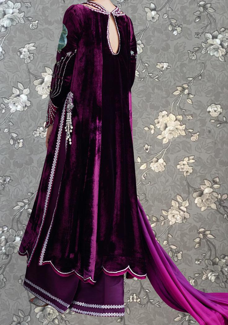 A person wearing a long, purple velvet dress with intricate embroidery and a matching purple skirt, standing against a gray floral background.