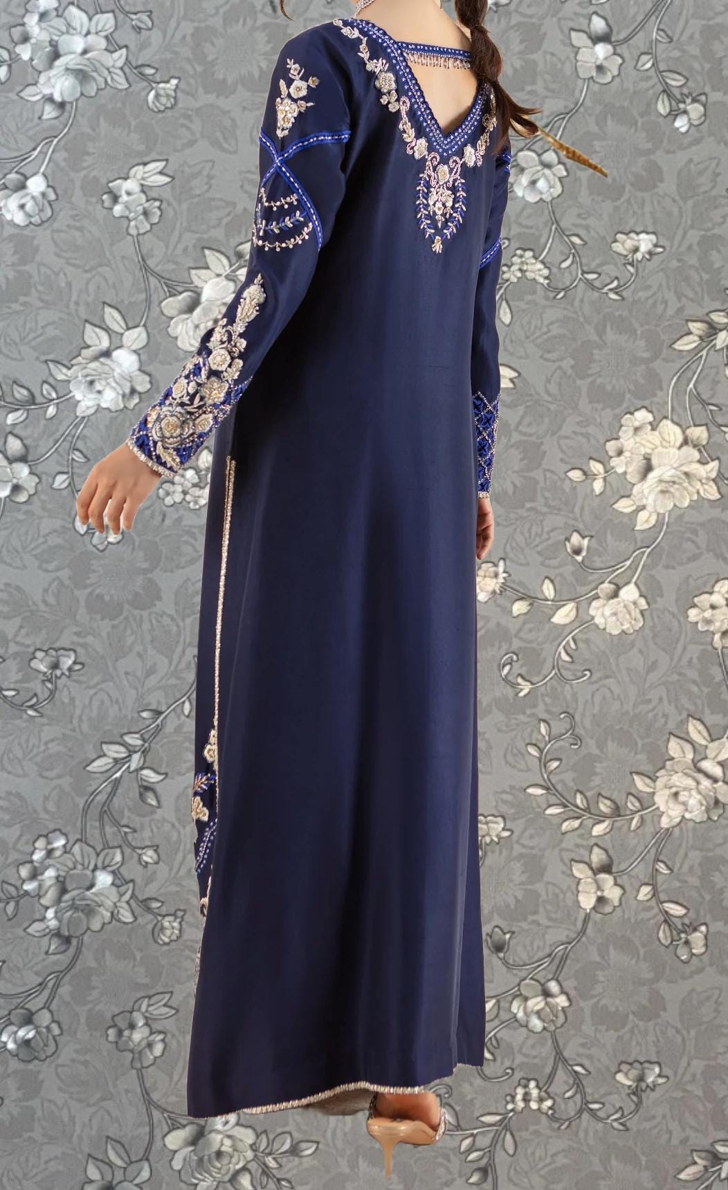 A person wearing a long, navy blue dress with intricate embroidery and floral patterns on the sleeves and back.