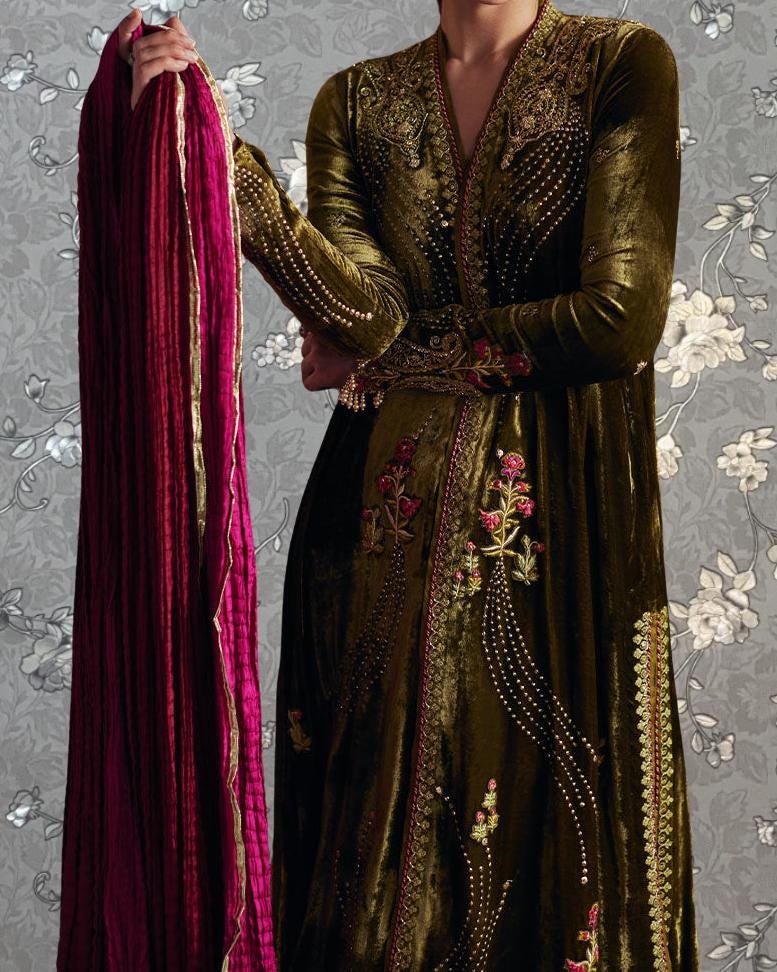 A person wearing an ornate, gold-colored dress with intricate embroidery and floral patterns, holding a long, red fabric draped over their shoulder.