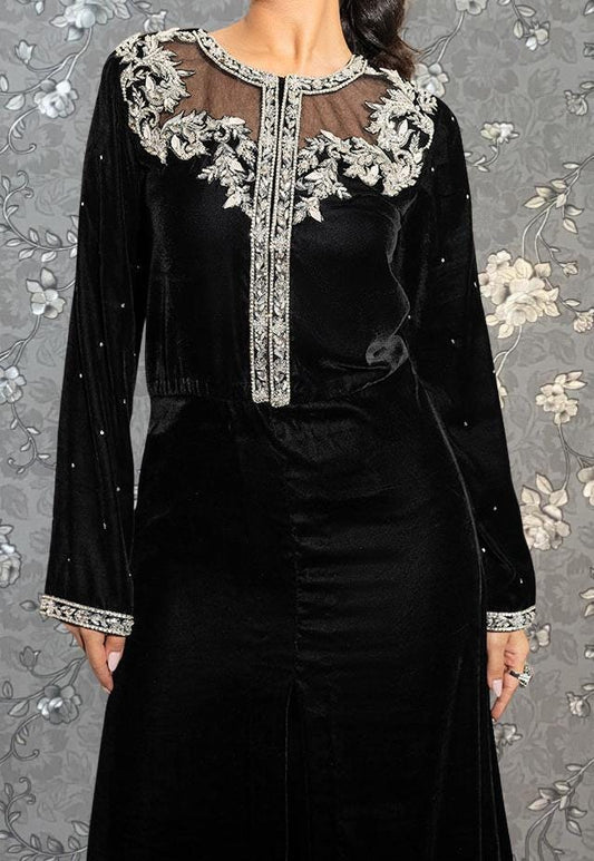 A woman wearing a long black dress with intricate white embroidery and a sheer overlay.
