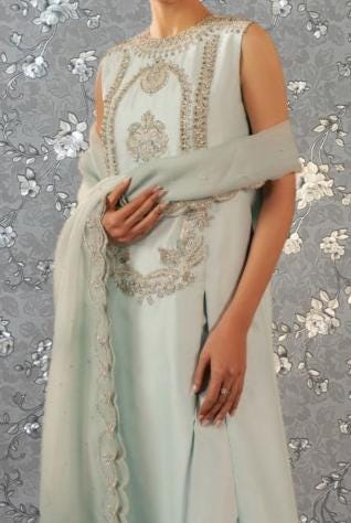 A woman wearing a light blue dress with intricate embroidery and a matching shawl draped over her shoulders.