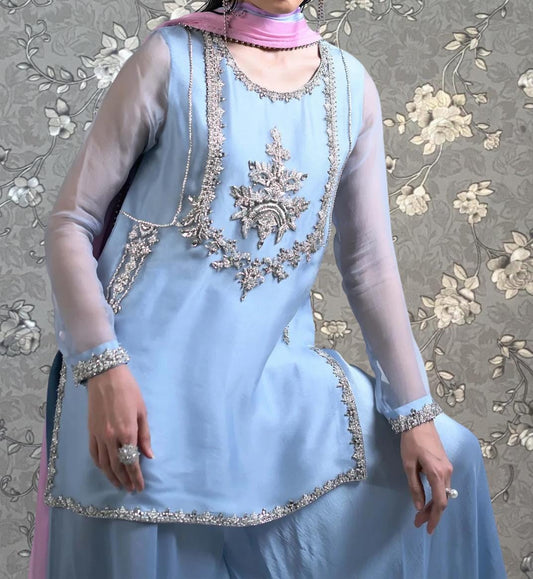 A woman wearing a blue dress with intricate silver embroidery and a pink scarf around her neck.