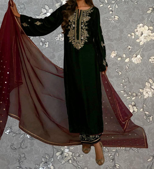 A woman wearing a long black dress with gold embroidery and a matching red shawl stands against a gray floral background.