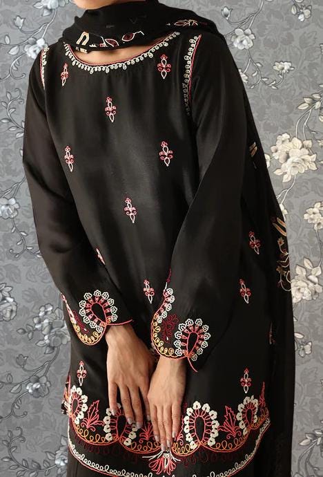 A person wearing a black dress with intricate embroidered patterns in red and gold.