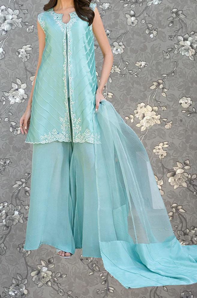 A woman wearing a turquoise dress with a long train, standing against a gray floral background.