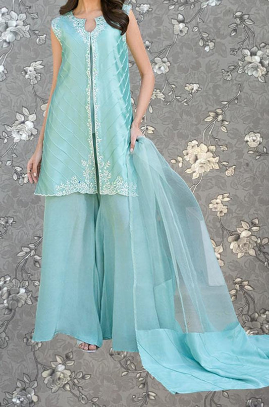 A woman wearing a turquoise dress with a long train, standing against a gray floral background.