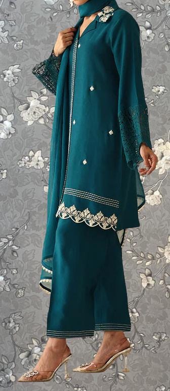 A woman wearing a teal green dress with lace sleeves and a matching skirt, standing against a gray floral background.