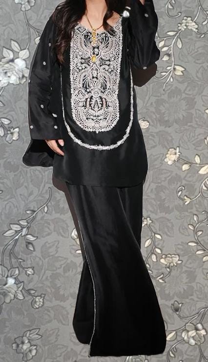 A woman wearing a black dress with a white floral pattern on the top and a long skirt.