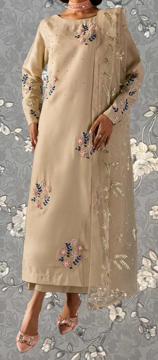 A woman wearing a long, beige dress with floral embroidery and a matching shawl.