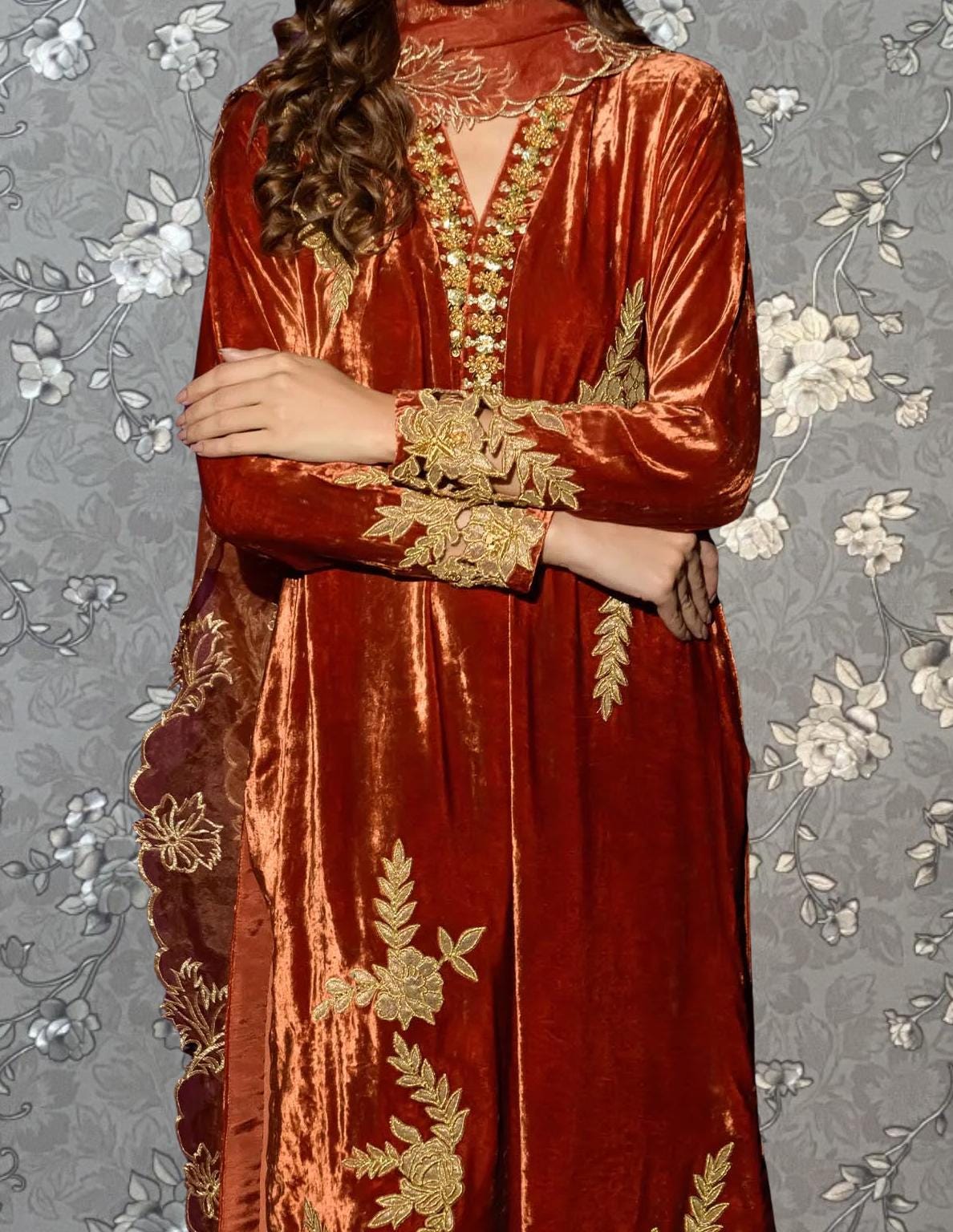 A person wearing a long, red velvet dress with gold embroidery and floral patterns.