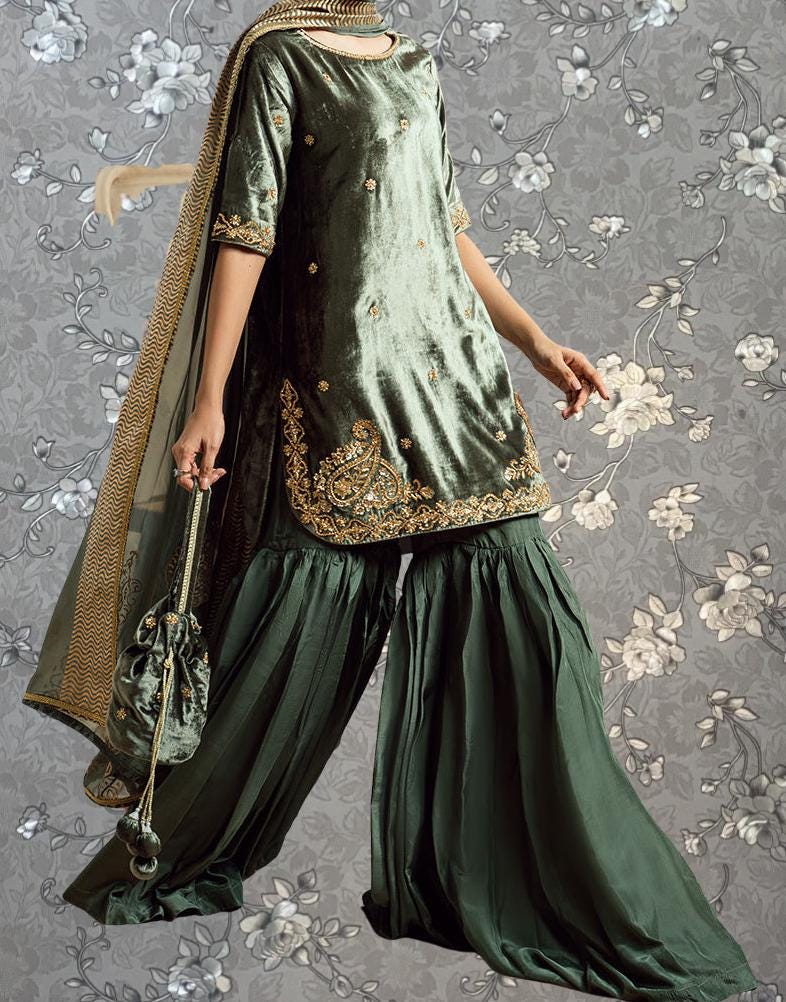 A person wearing a green and gold dress with a matching green skirt, standing against a gray floral background.