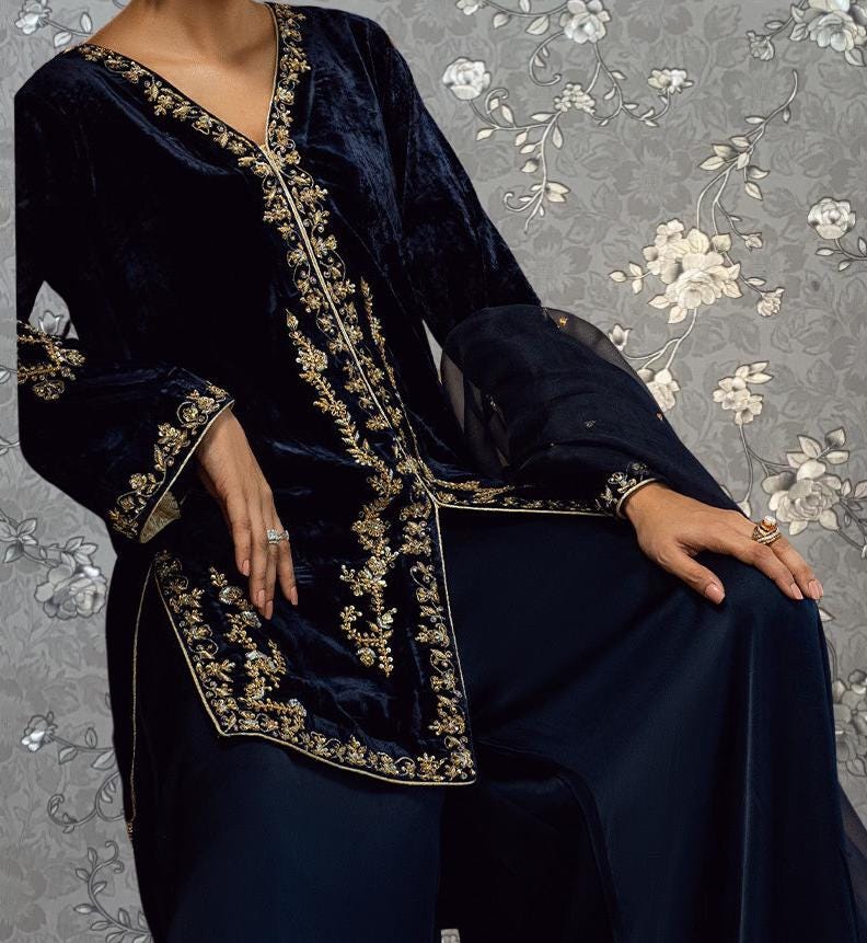A person wearing a long, dark blue velvet dress with gold embroidery and a matching jacket.