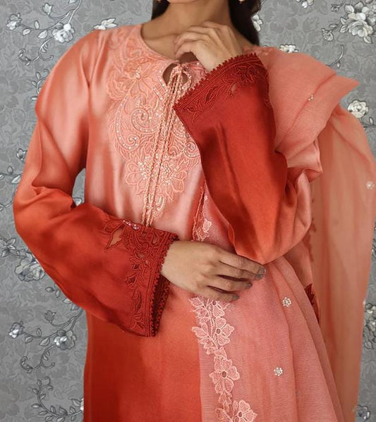 A woman wearing a peach-colored dress with intricate embroidery and lace details, posing against a gray floral background.