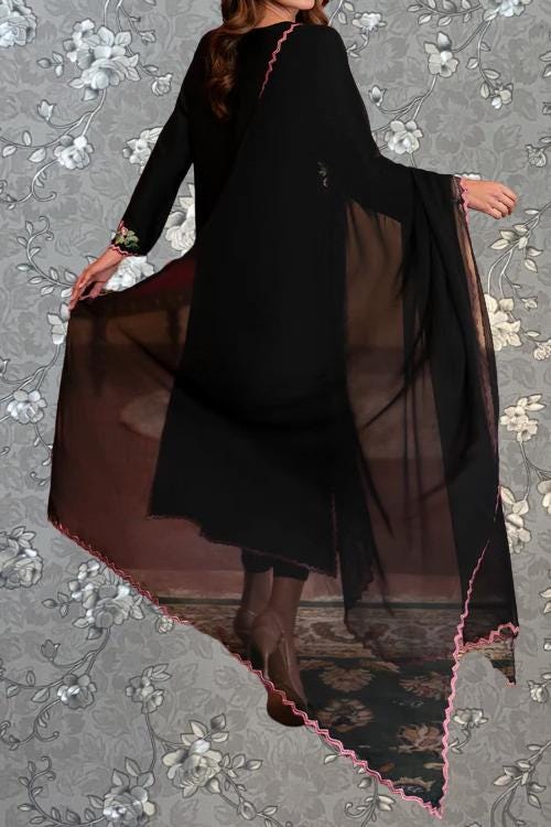 A woman wearing a long black dress with a sheer, flowing skirt and a pink trim, posing against a floral background.