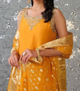 A woman wearing a bright yellow dress with gold accents, posing against a gray floral background.