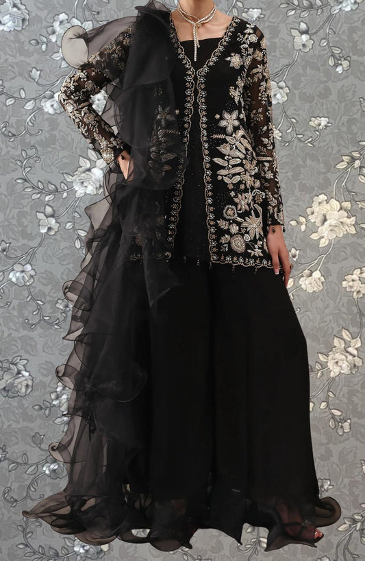 A woman wearing a black and gold dress with a long, flowing skirt and a sheer, ruffled jacket.