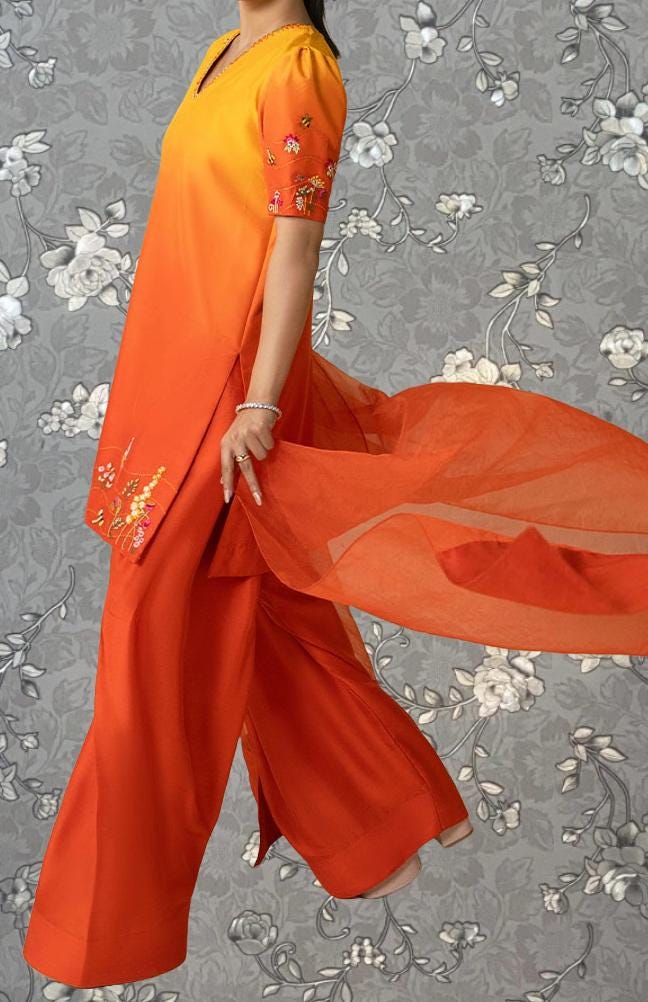 A person wearing a vibrant orange dress with floral embroidery is shown against a gray floral background.