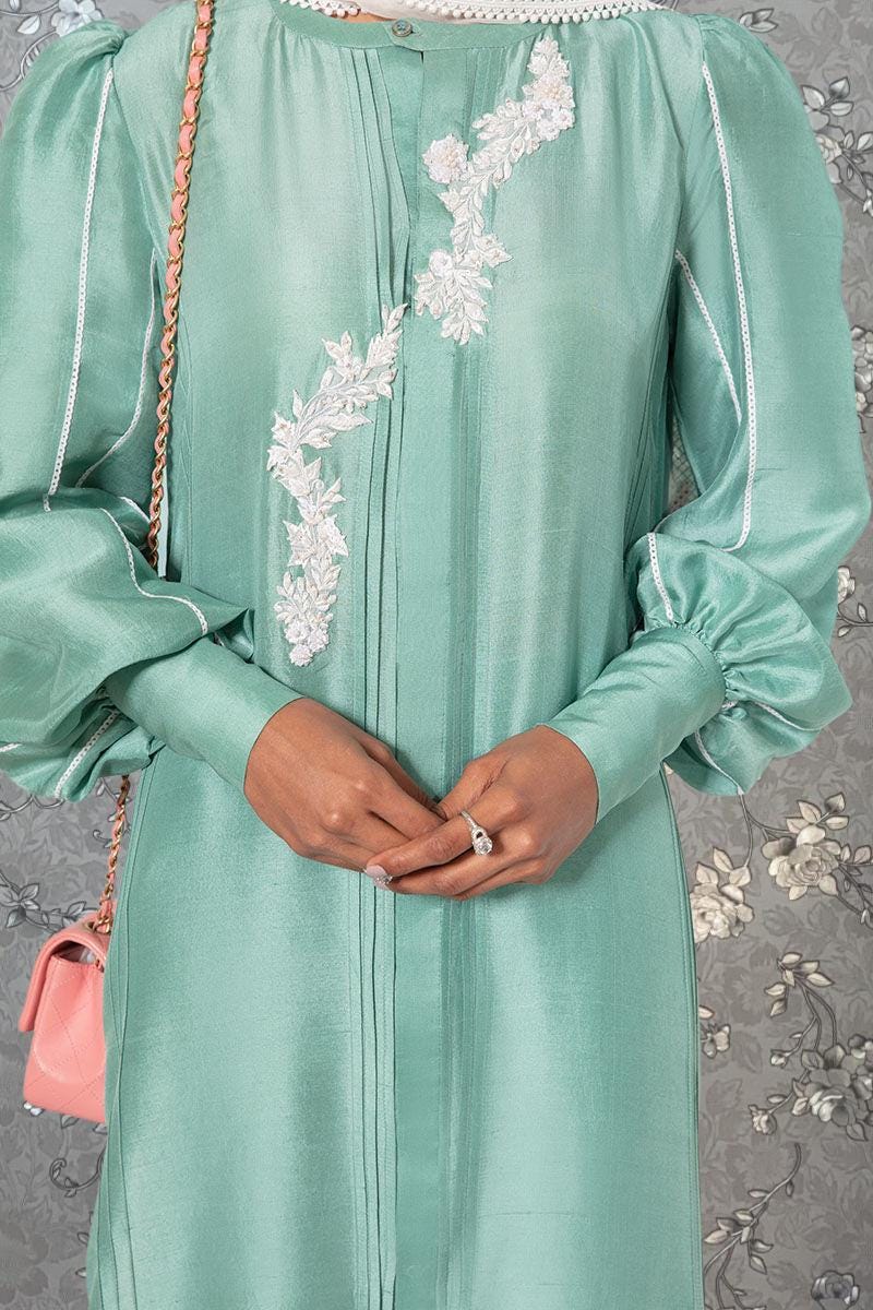 A person wearing a mint green dress with white floral embroidery on the sleeves and collar.