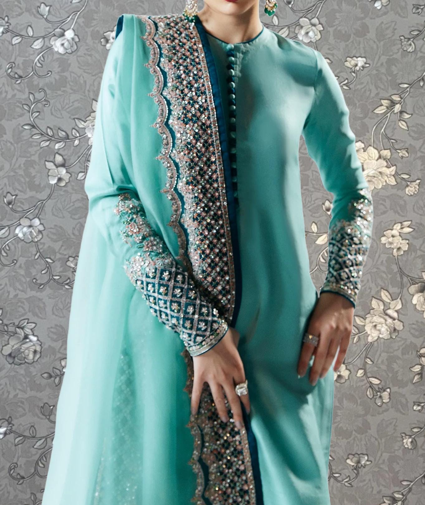A woman wearing a turquoise dress with intricate embroidery and a matching turquoise shawl.