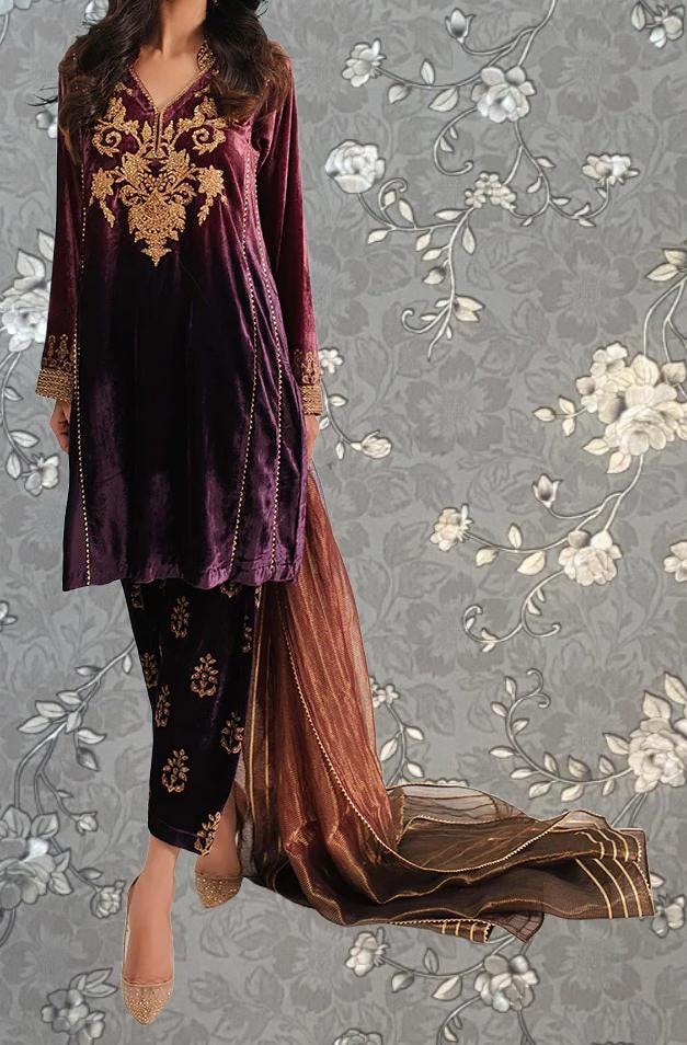 A woman wearing a purple velvet dress with gold embroidery and a matching skirt, standing against a gray floral background.