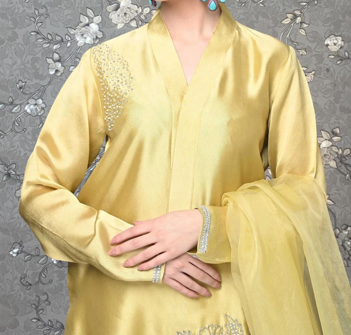 A person wearing a yellow dress with a gold embellished design on the shoulder and a matching gold shawl draped over the shoulder.