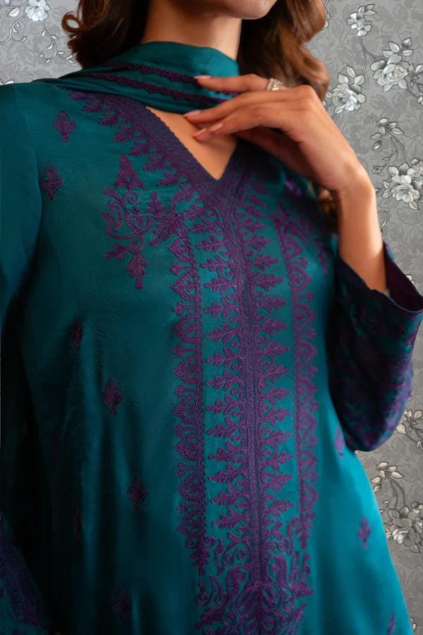 A close-up of a woman wearing a teal-colored dress with intricate purple embroidery.