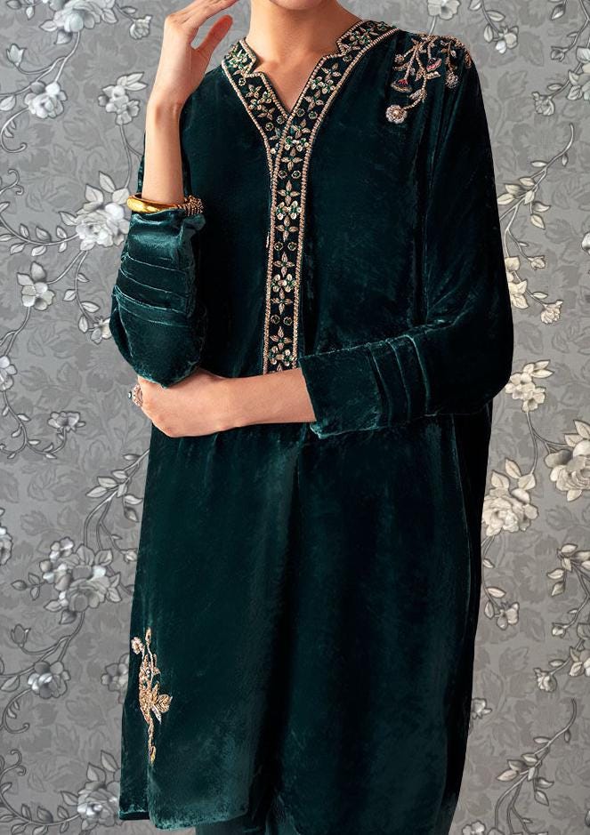 A person wearing a dark green velvet dress with gold embroidery and a floral pattern on the sleeves.