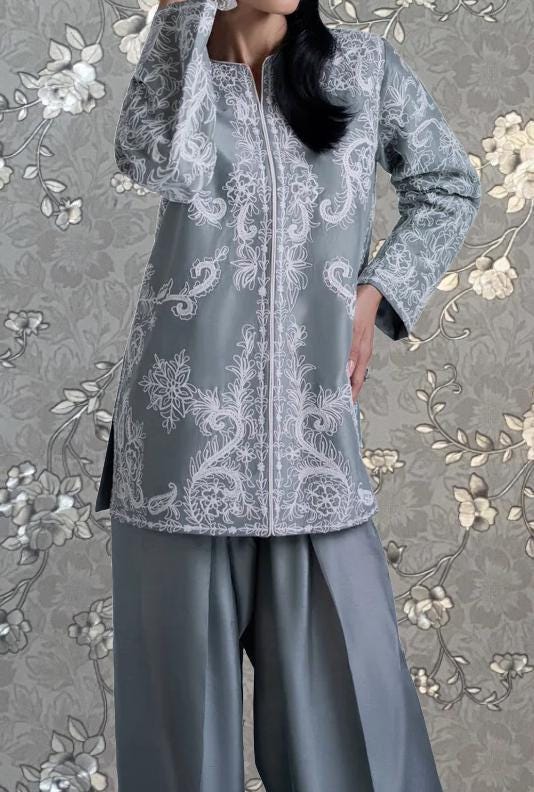 A woman wearing a gray and white patterned dress with a floral design, standing against a gray floral background.