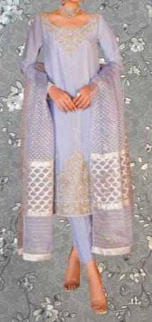 A woman wearing a lavender and gold patterned dress with a matching shawl, standing against a gray floral background.