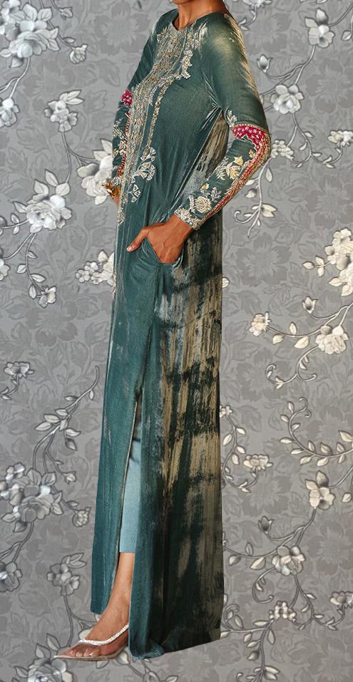 A person wearing a long, green dress with intricate embroidery and floral patterns stands against a gray floral background.