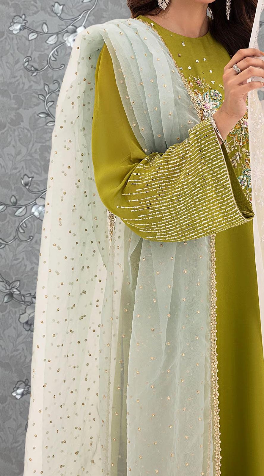 A close-up of a person wearing a green and white dress with a white and gold patterned shawl draped over their shoulders.