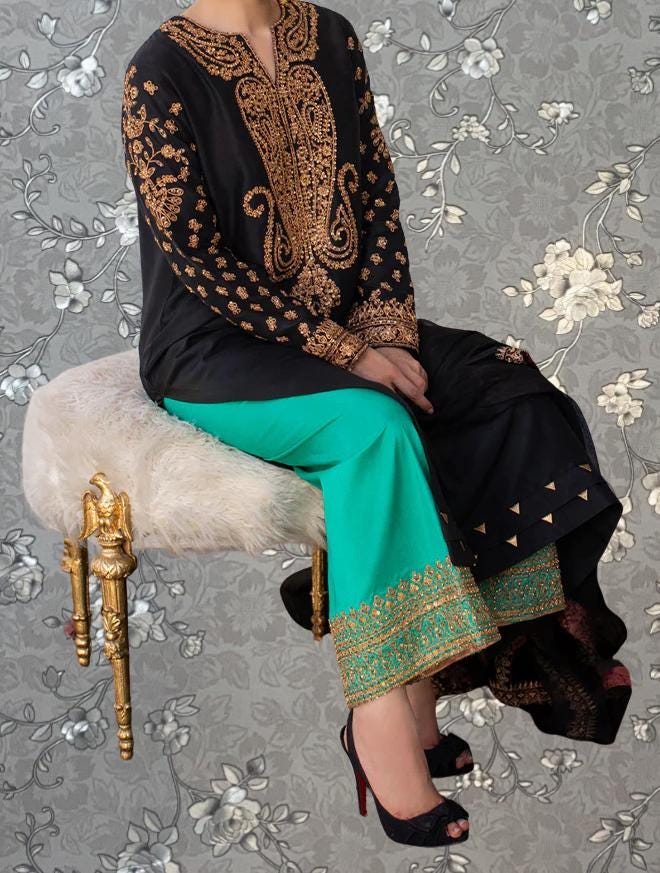 A person wearing a black and gold dress with intricate embroidery, sitting on a white fur-covered chair with gold accents.