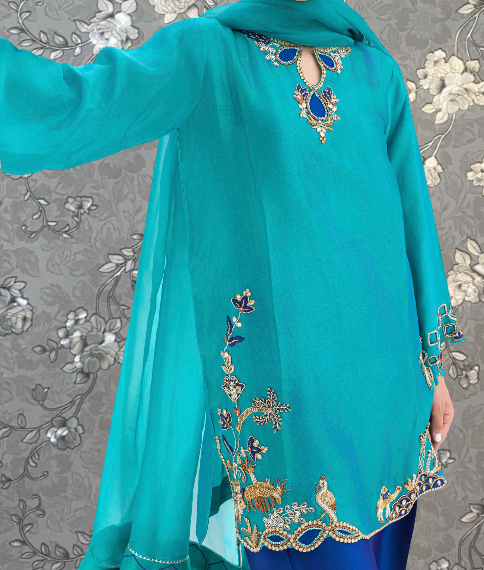 A person wearing a turquoise dress with intricate embroidered designs on the sleeves and hem.