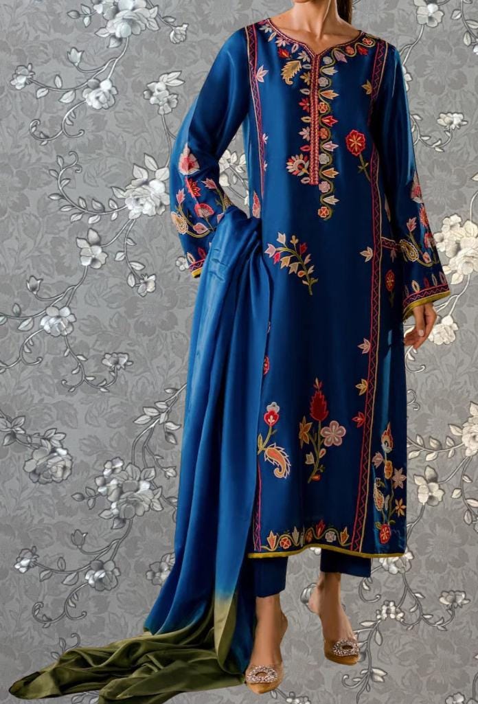 A woman wearing a blue dress with intricate floral embroidery and a matching blue shawl.