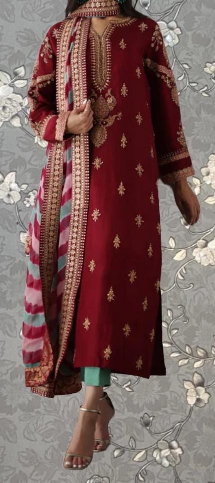 A woman wearing a red and gold embroidered dress with a matching shawl, standing against a gray floral background.