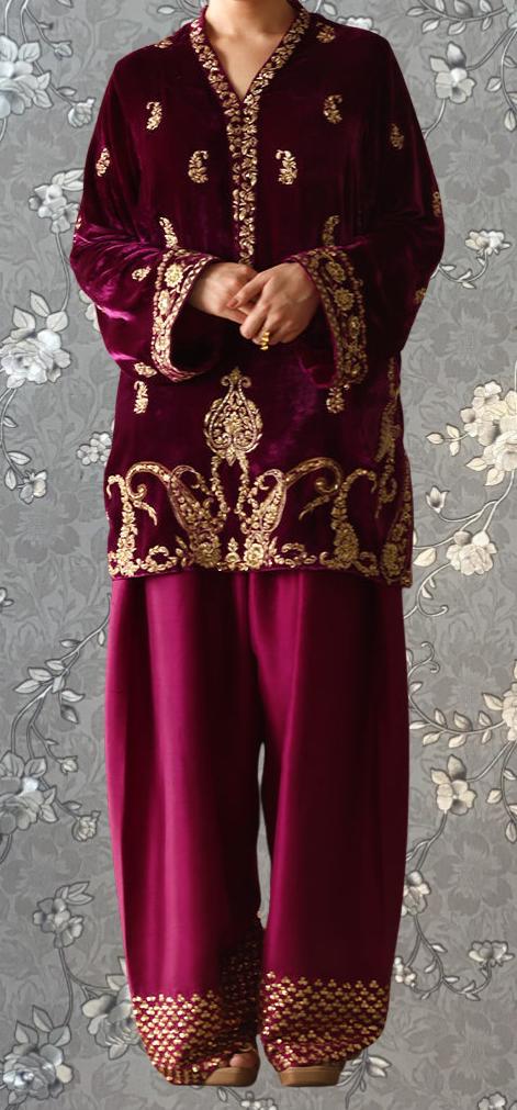 A person wearing a burgundy velvet dress with gold embroidery and a matching burgundy velvet blazer.