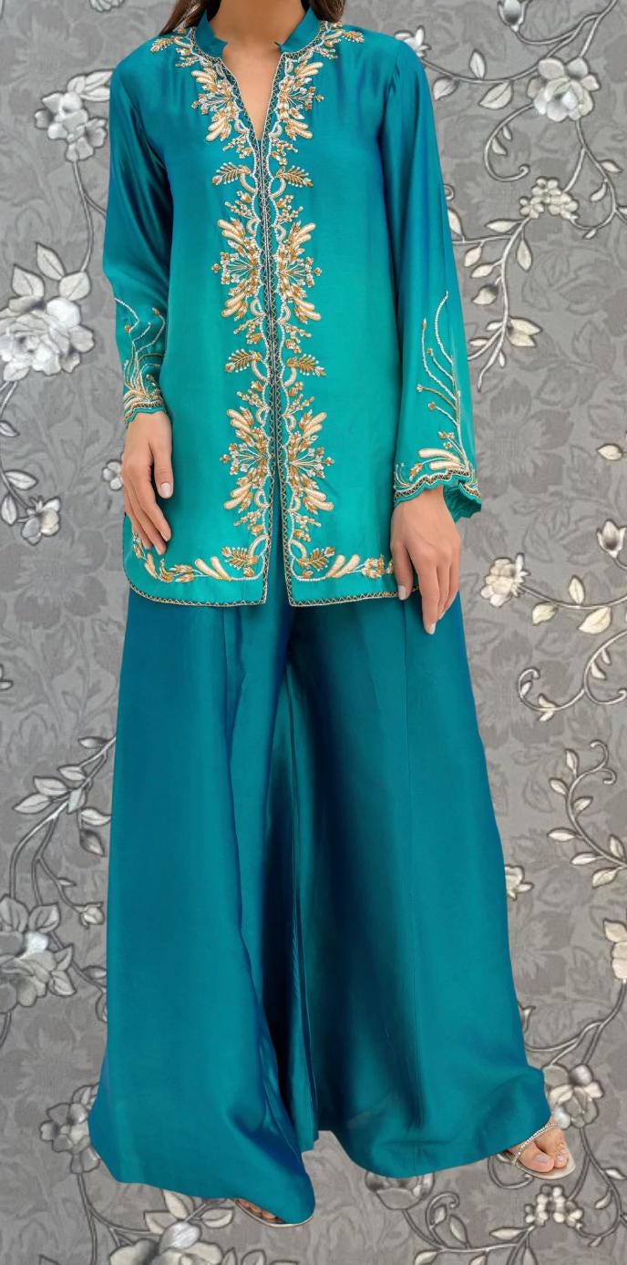 A woman wearing a teal-colored dress with gold embroidered patterns on the sleeves and collar.