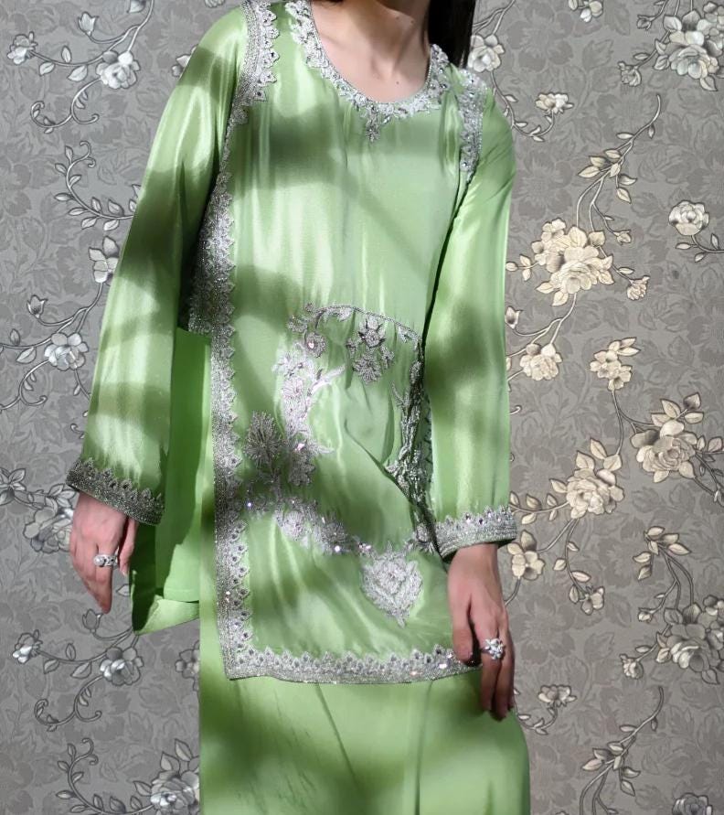 A person wearing a green dress with intricate embroidery and a floral pattern on the background.