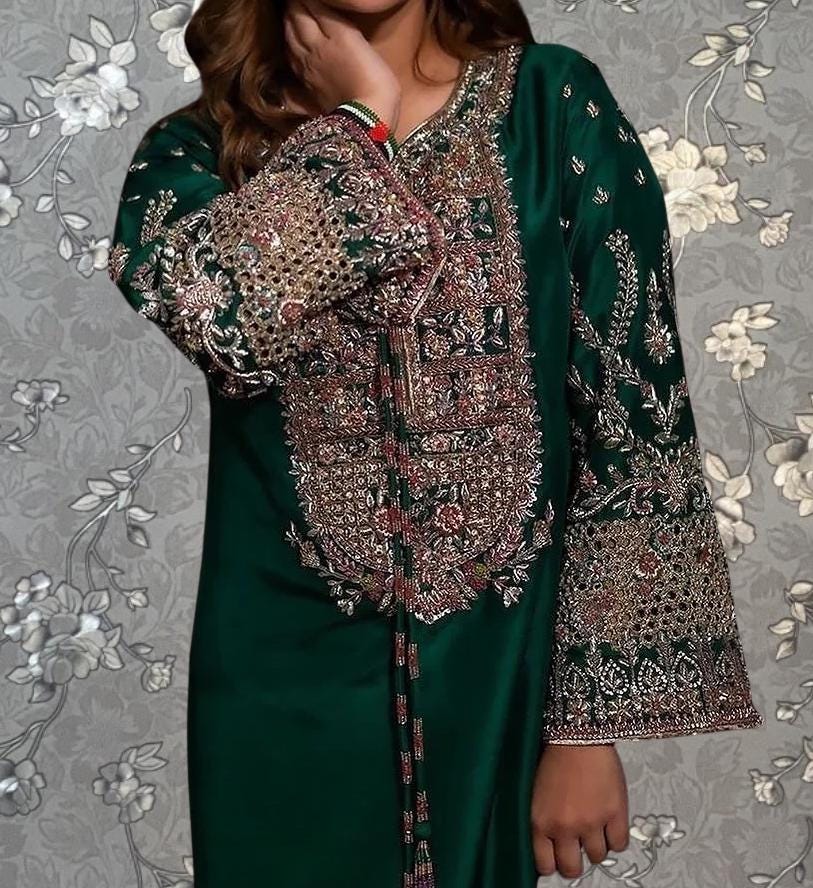 A woman wearing a green dress with intricate embroidery and patterns on the sleeves and collar.