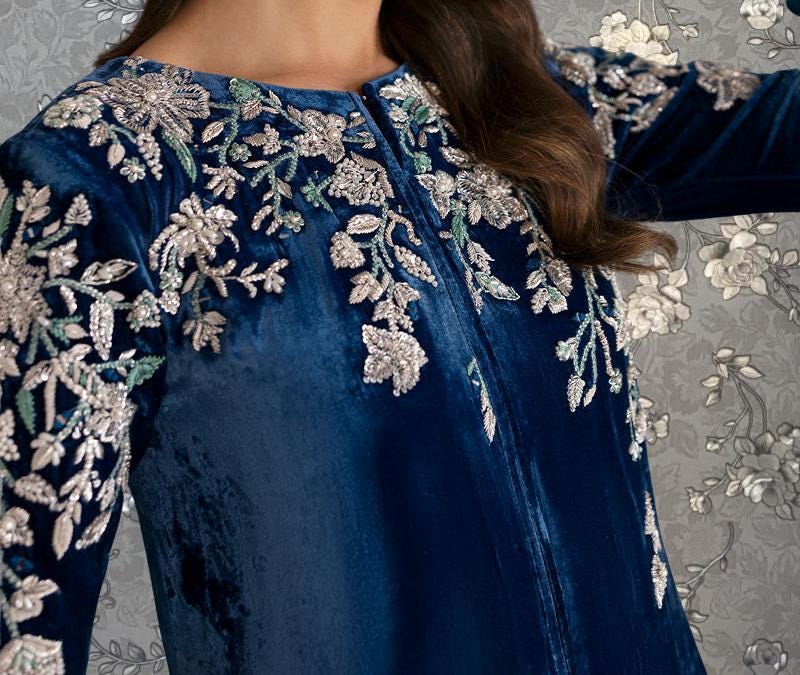 A close-up view of a woman wearing a blue velvet dress with intricate floral embroidery on the sleeves and collar.