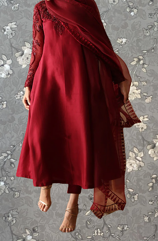 A woman wearing a long red dress with lace sleeves and a matching red shawl, standing against a gray floral background.